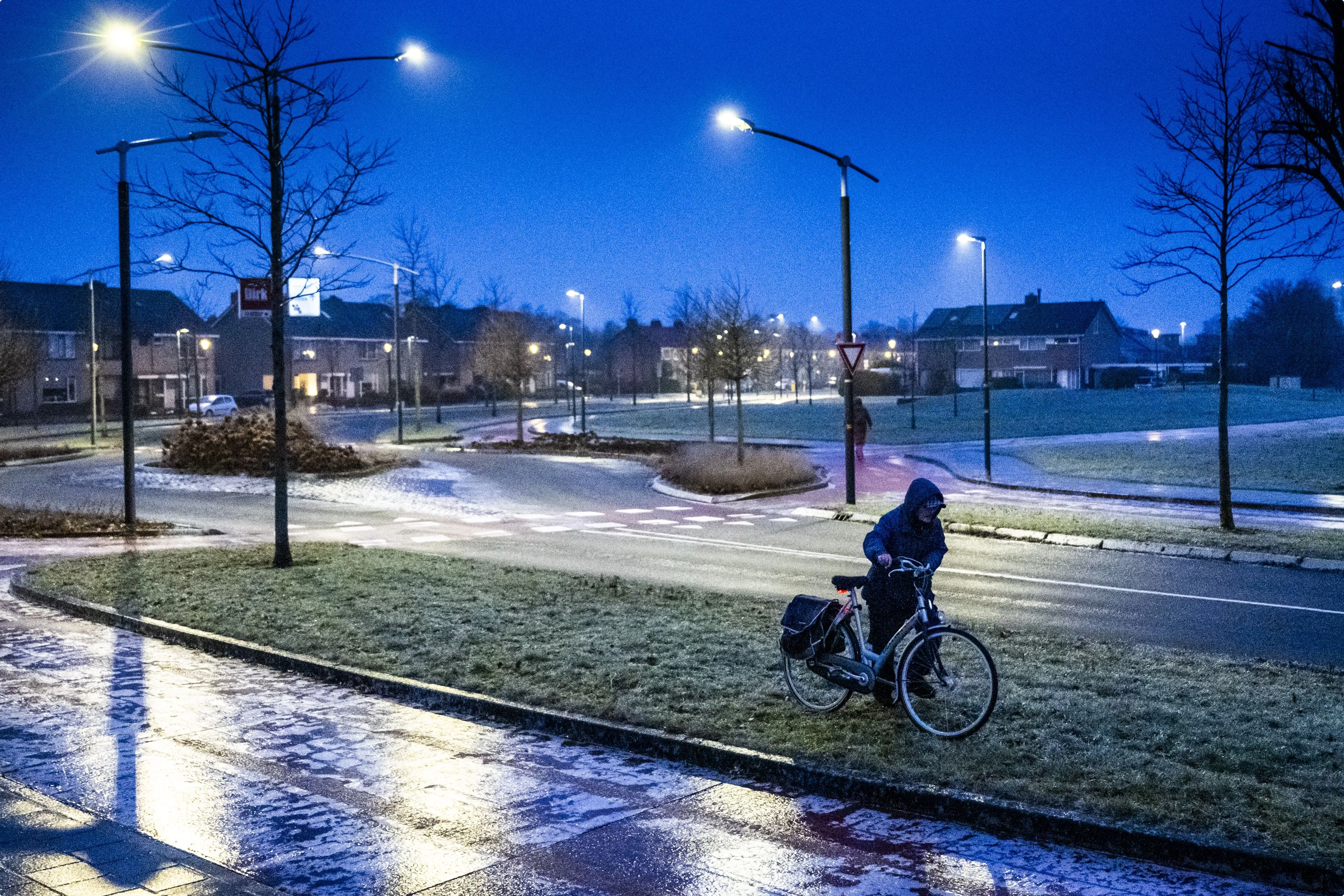 Een man loopt met zijn fiets aan de hand door het gras waar het niet glad is. Beeld: ANP