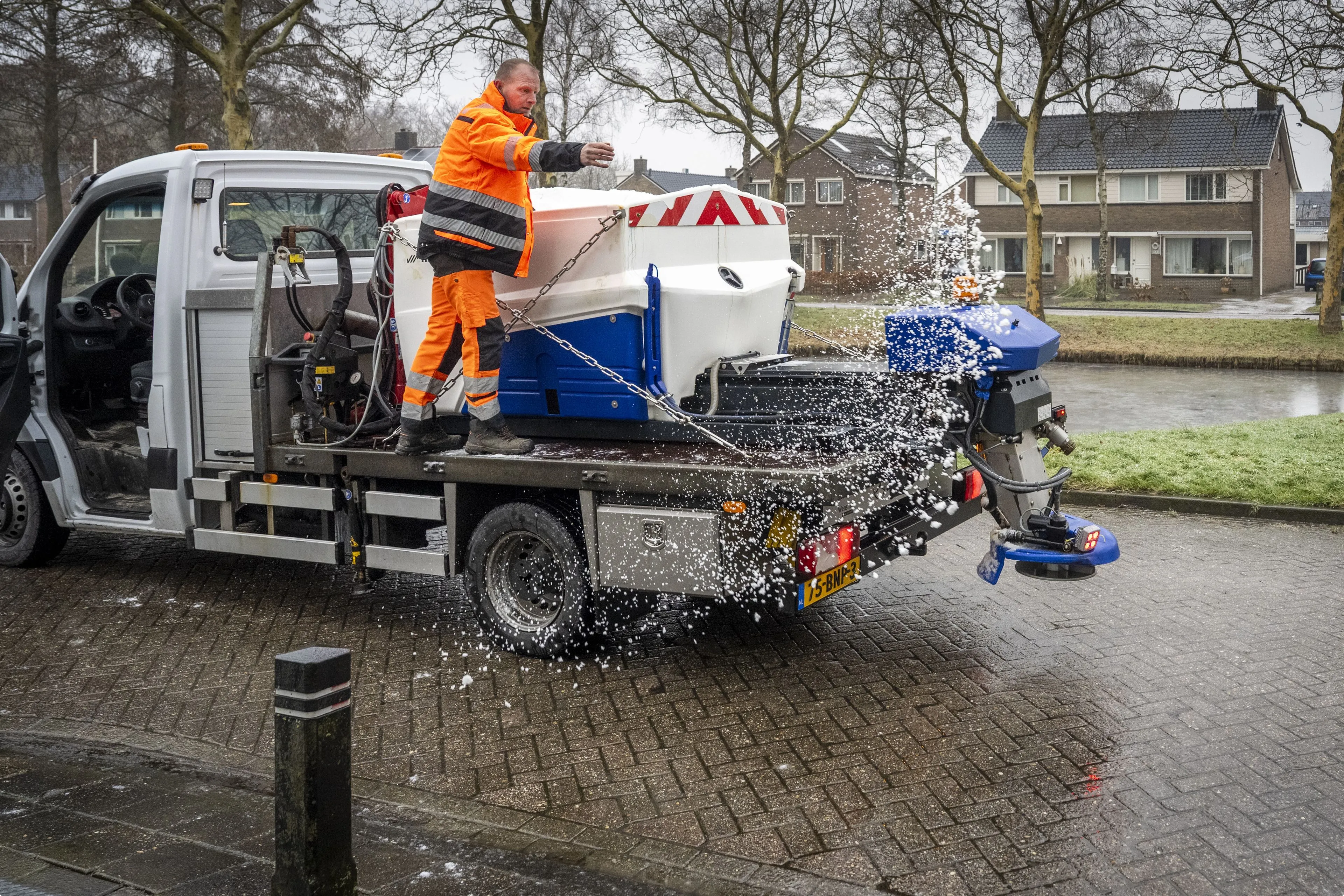 Een gemeenteambtenaar probeert met wat zout een vastzittend busje te helpen. Beeld: ANP